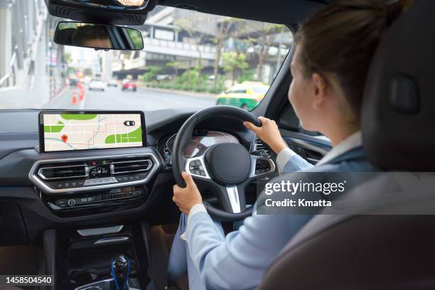 back view of young female driver sitting at steering wheel and looking gps navigation screen during road trip. - gps stock-fotos und bilder