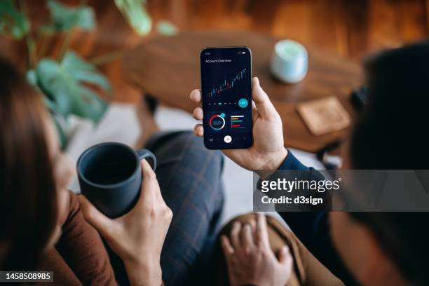 young asian couple managing finance and investment online, analyzing stock market trades with mobile app on smartphone. making financial plans. banking and finance, investment, financial trading, mobile banking concept - talking phone stock pictures, royalty-free photos & images