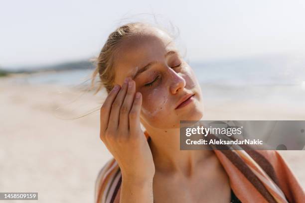 teenage girl applying sunscreen at the beach - suncream stock pictures, royalty-free photos & images