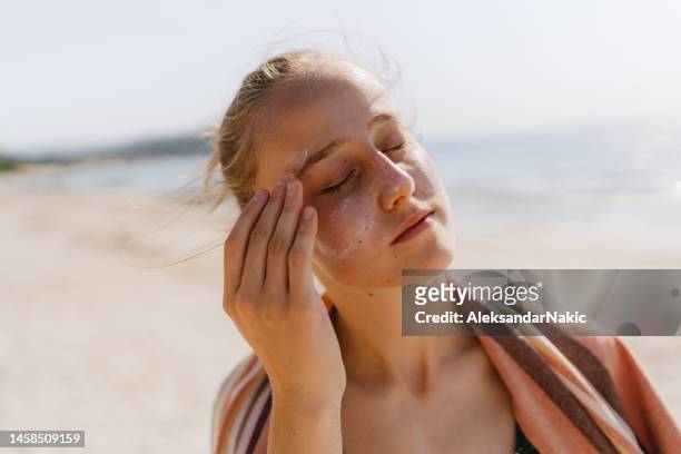 teenage girl applying sunscreen at the beach - sunscreen imagens e fotografias de stock
