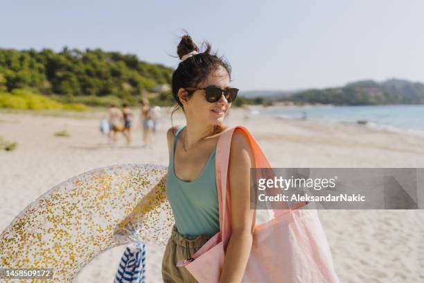 smiling young woman holding an inflatable ring - beach bag stockfoto's en -beelden