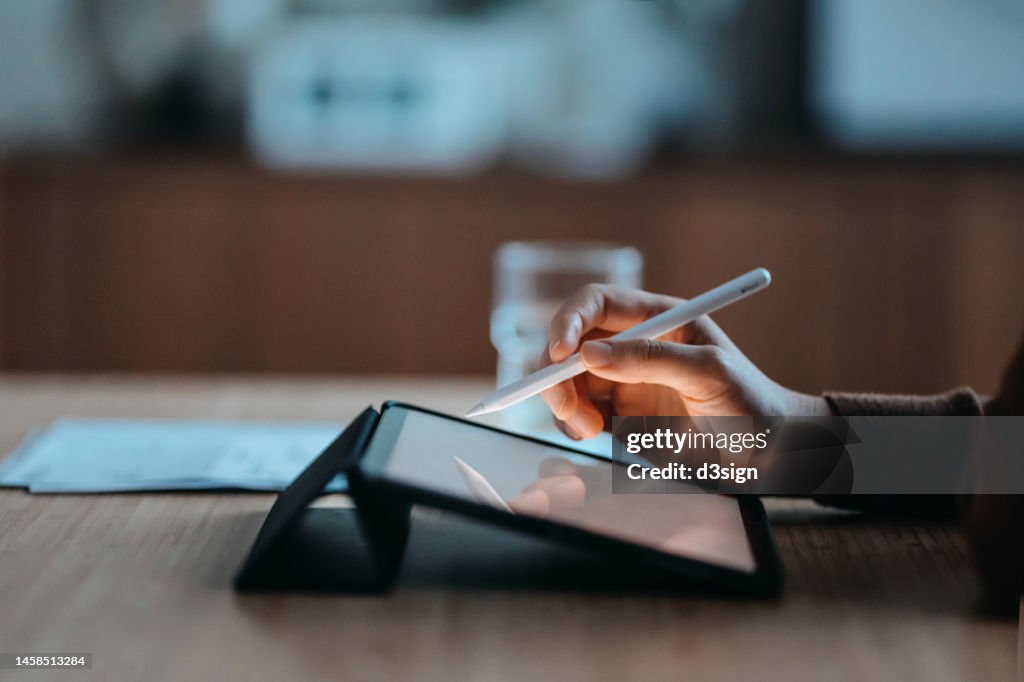 Side view, close up of a female hand using digital tablet with a pen while working from home. Lifestyle and technology