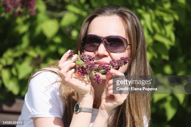 young cheerful woman in sunglasses relaxing outdoor and putting on blossom lilac twig for smile - older woman happy smile foto e immagini stock
