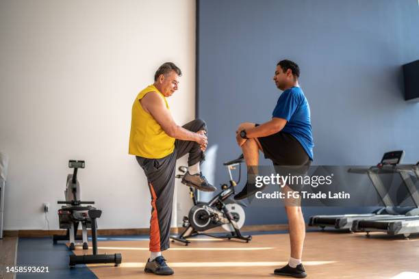 mature man stretching with the help of fitness instructor at the gym - warm up exercise indoor stock pictures, royalty-free photos & images