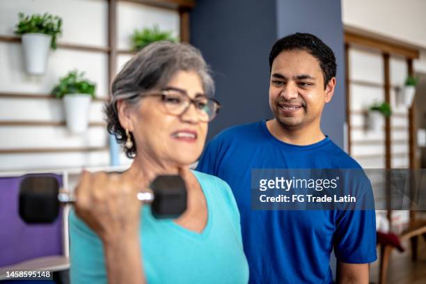 fitnesstrainer unterstützt ältere frauen beim gewichtheben im fitnessstudio - exercise room stock-fotos und bilder