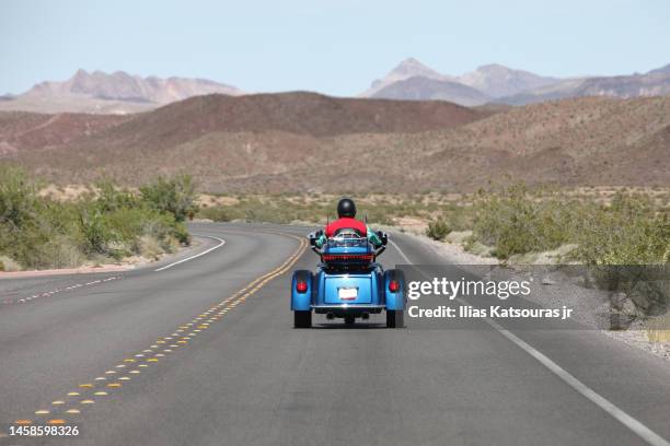 man rides tricycle on desert road - tricycle stock-fotos und bilder