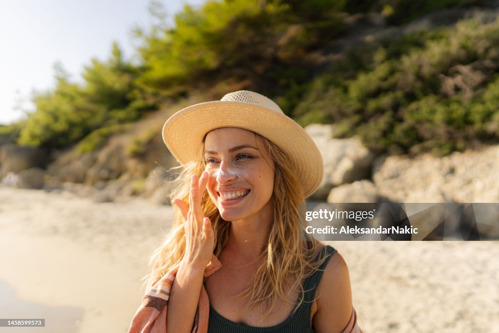 Junge Frau, die Sonnencreme am Strand aufträgt