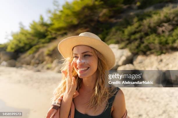 junge frau, die sonnencreme am strand aufträgt - suntan lotion stock-fotos und bilder