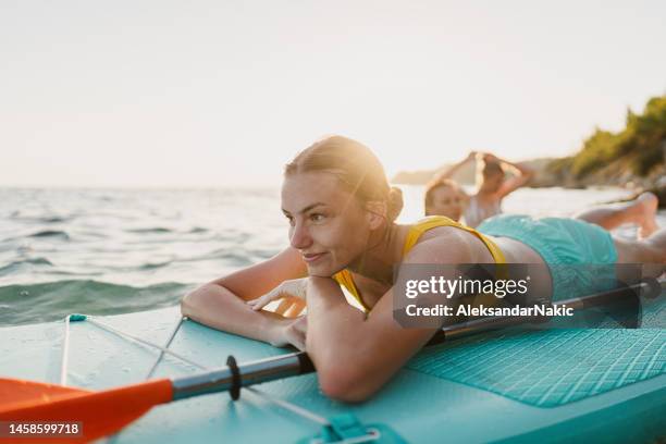 mujer joven de pie remando en la playa - deporte acuático fotografías e imágenes de stock