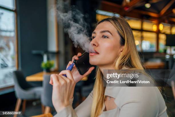 woman smokes disposable vape cigarette while talking on smart phone - electric cigarette stock pictures, royalty-free photos & images