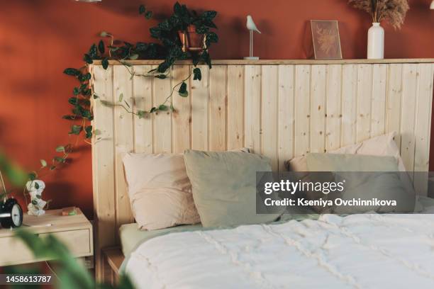 elegant and quiet bohemian room with cozy interior, wicker chair, pillows, cushions, green plants in flower pot, bed and rug on wooden floor - cechy stockfoto's en -beelden