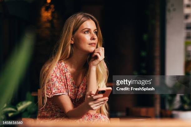 a happy beautiful blonde businesswoman using her mobile phone while sitting at the cafe - charming stockfoto's en -beelden