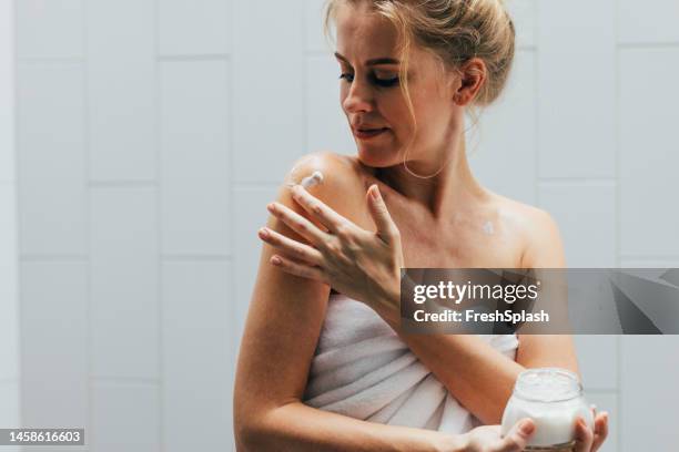 a happy beautiful blonde woman applying some creme on her body after having a shower - skin cream stock pictures, royalty-free photos & images