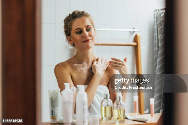 a happy beautiful blonde woman applying some creme on her body after having a shower - woman shower bath imagens e fotografias de stock