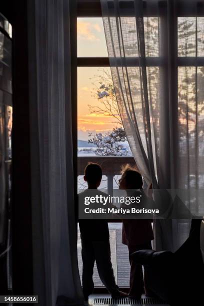 a boy and a girl stand at a large panoramic window and admire the sunset. - house golden hour stock pictures, royalty-free photos & images