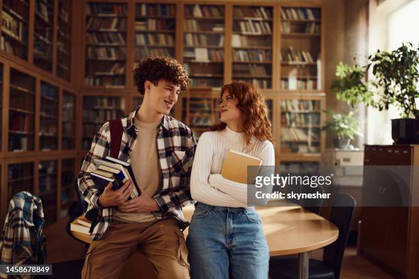 felice coppia del liceo che parla in biblioteca. - happy student girl foto e immagini stock