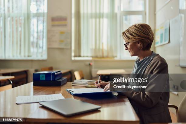 female teacher writing her plans in the classroom. - female lecturer stock pictures, royalty-free photos & images