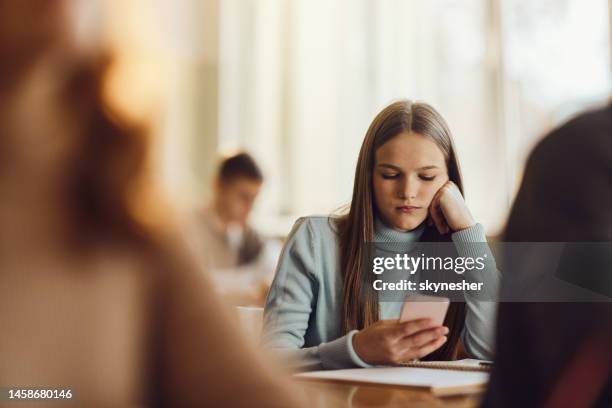 gelangweilte schülerin benutzt handy in einer klasse in der schule. - schüler smartphone stock-fotos und bilder