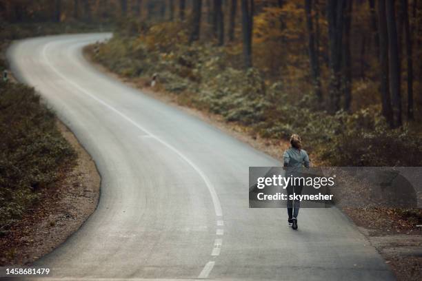 rear view of a female athlete jogging on the road in nature. - corrida de rua imagens e fotografias de stock