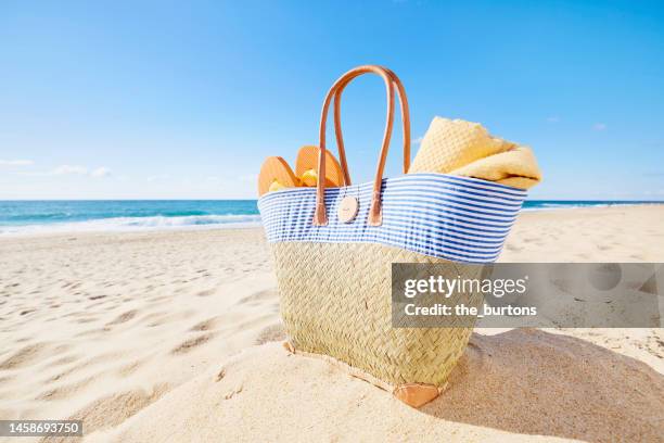 beach bag with blanket and flip-flops at beach and sea against blue sky - beach bag foto e immagini stock