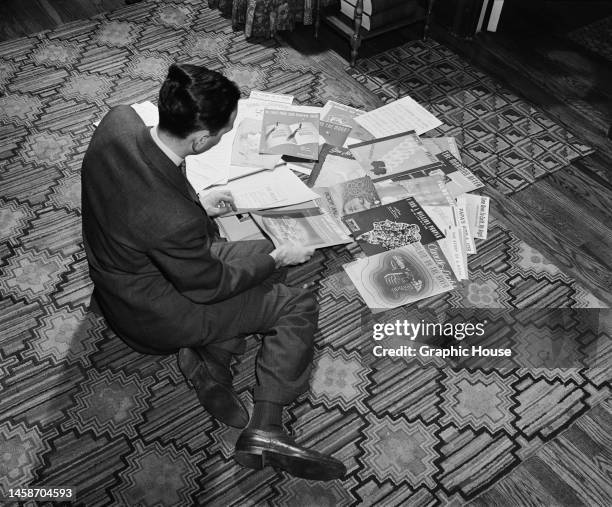 High angle view of American composer and lyricist Robert Sour looking at sheet music for his compositions on the floor in front of him , United...