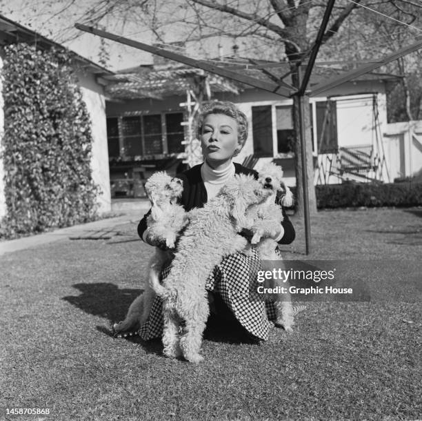 America dancer and actress Vera-Ellen , wearing black cardigan over a white turtleneck and a checked skirt, with three small dogs in a garden of a...