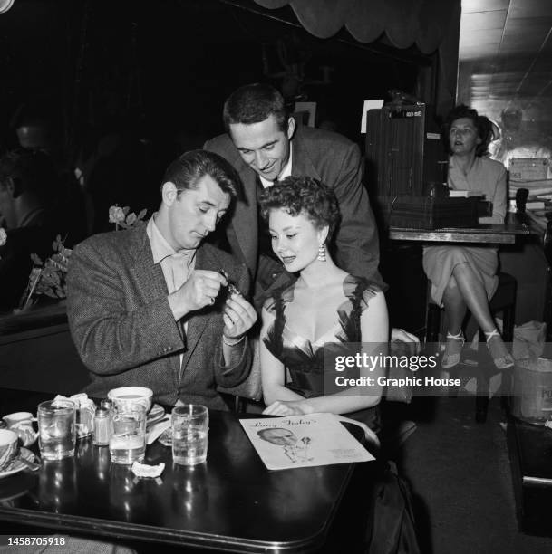 American actor Robert Mitchum examining the wristwatch of American actress, singer, dancer and singer Mitzi Gaynor with her husband, American film...