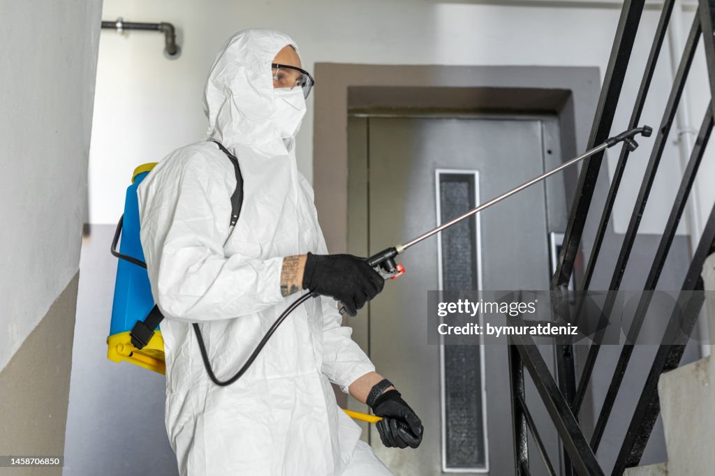A man wearing protective suit and disinfecting and spraying with spray chemicals residential building