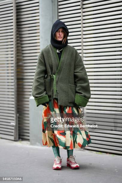 Guest wears a black hoodie, a black turtleneck wool pullover, a dark green wool oversized coat, a beige / green / orange print pattern ruffled midi...
