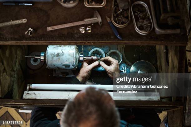 jeweler making a triskele silver pendant necklace with a cutting machine in his workshop - jeweller stock pictures, royalty-free photos & images