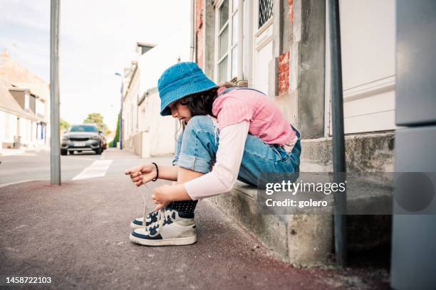 girl with hat sitting on steps tying shoes - 13 years old girl in jeans stock pictures, royalty-free photos & images