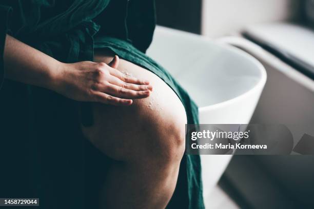 woman in bathroom applying scrub on legs. - cellulite stock pictures, royalty-free photos & images