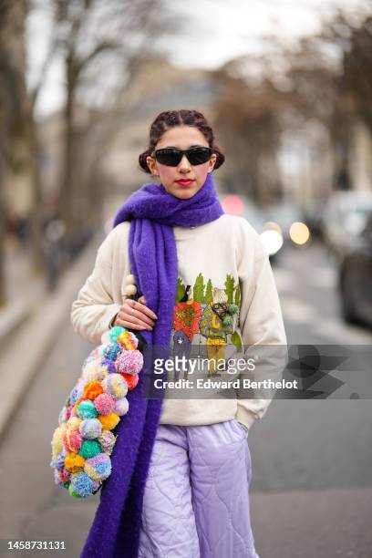 Guest wears black sunglasses, a neon purple wool long scarf, a white latte with orange / yellow / green embroidered landscape pattern pullover, a...