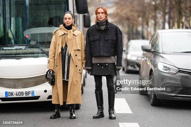 Guest wears a black turtleneck pullover, a black short dress, black tights, a beige hoodie long trench coat, a black shiny varnished with white sheep...