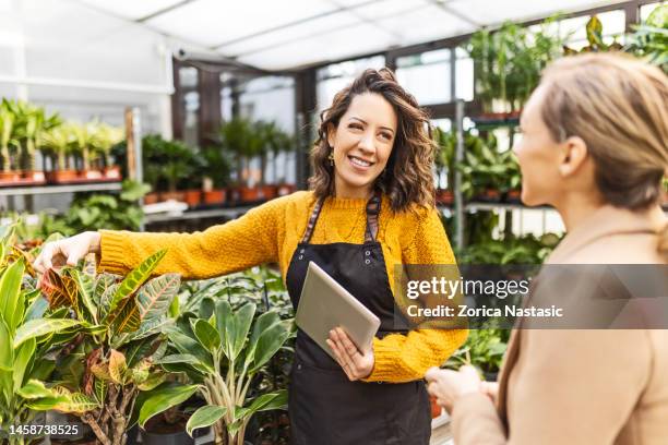 lächelnde frau in einem gartencenter im gespräch mit einem angestellten - natuurkunde stock-fotos und bilder