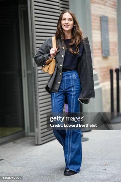 Guest wears a black shirt, a dark gray wool buttoned jacket, navy blue high waist flared pants, a brown shiny leather shoulder bag, a gold Love ring...