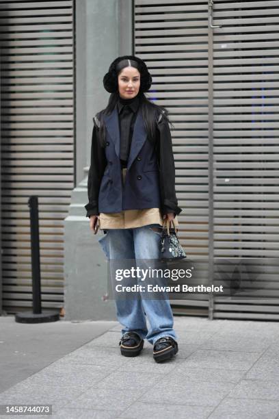 Guest wears a black fluffy ear muffs, a black turtleneck pullover, a black oversized shirt, a navy blue sleeveless blazer jacket, a beige short...