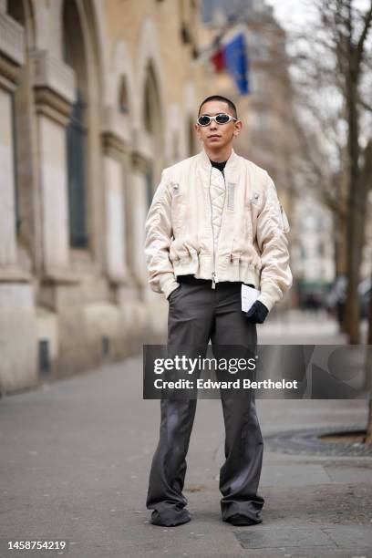 Guest wears silver sunglasses, a black t-shirt, gold earrings, a white quilted zipper bomber coat, dark gray flared suit pants, black sneakers, black...