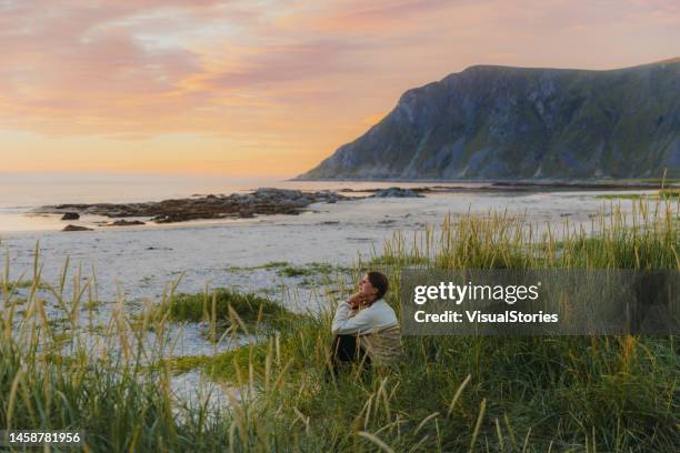 seitenansicht einer weiblichen reisenden, die den sonnenuntergang am malerischen bergstrand auf den lofoten betrachtet - nordeuropa stock-fotos und bilder