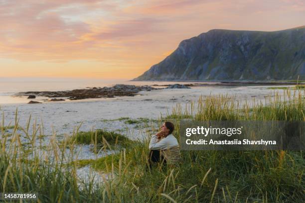 side view of a woman traveler contemplating sunset by the scenic mountain beach on lofoten islands - norway landscape stock pictures, royalty-free photos & images