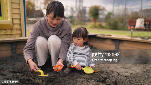 small girl playing with sand together with her mother in public park - sand pail and shovel stock pictures, royalty-free photos & images