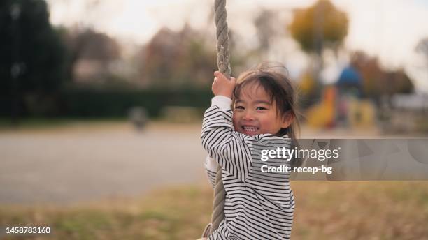 kleines mädchen spielt gerne mit gleitseil im öffentlichen park - schaukel stock-fotos und bilder
