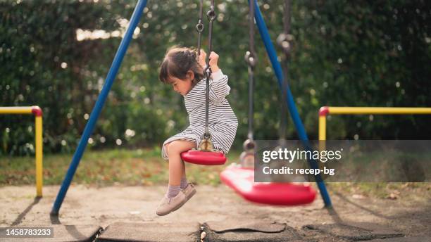 piccola ragazza che si siede sull'altalena da sola nel parco pubblico - altalena foto e immagini stock