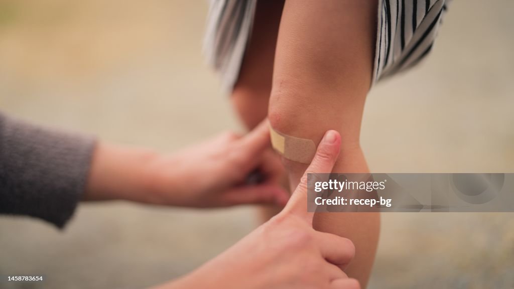 Mother covering wound of her small daughter with bandaid in public park