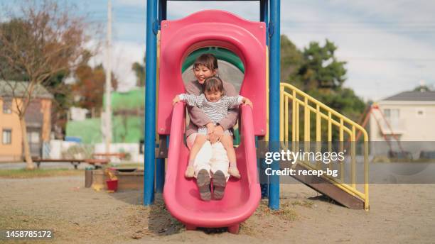 small girl playing with her mother in public park and sliding on slide - kid looking down stock pictures, royalty-free photos & images