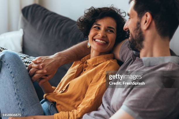 a happy beautiful couple sitting on the cozy sofa at home and relaxing - happy couple at home stock pictures, royalty-free photos & images