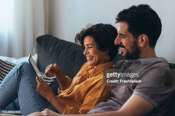 happy couple browsing the web on a tablet - mid adult couple stock pictures, royalty-free photos & images