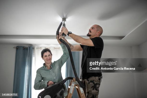 man with electric drill and crown is preparing to drill holes in the plasterboard ceiling to place led lamps with portholes, while the woman sucks up the dust with the vacuum cleaner, hole saw - vacuum cleaner woman stockfoto's en -beelden