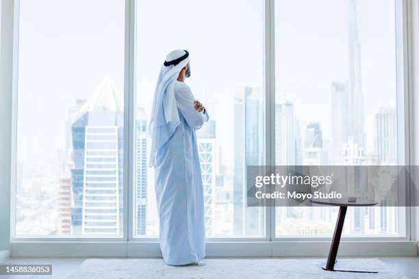 vue latérale d’un homme d’affaires arabe regardant par la fenêtre dans un bureau moderne - foulard couvre chef photos et images de collection