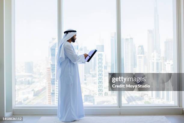 seitenansicht eines arabischen geschäftsmannes mit digitalem tablet neben fenster im modernen büro - emirati at work stock-fotos und bilder